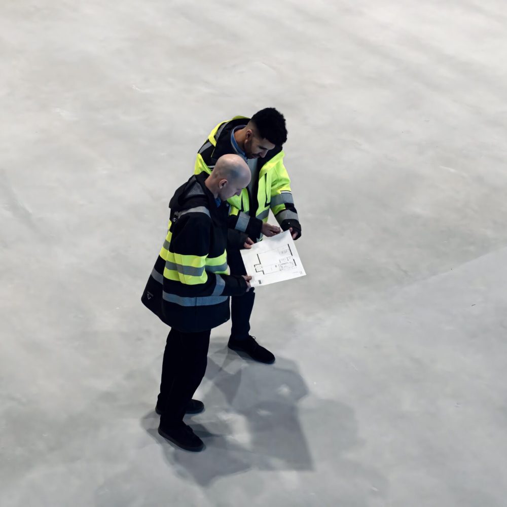 Arkitekter på byggplats inför färdigställande av sporthall – Hallkonsulten Arkitekter från Hallkonsulten granskar ritningar på byggplats inför färdigställande av sporthall