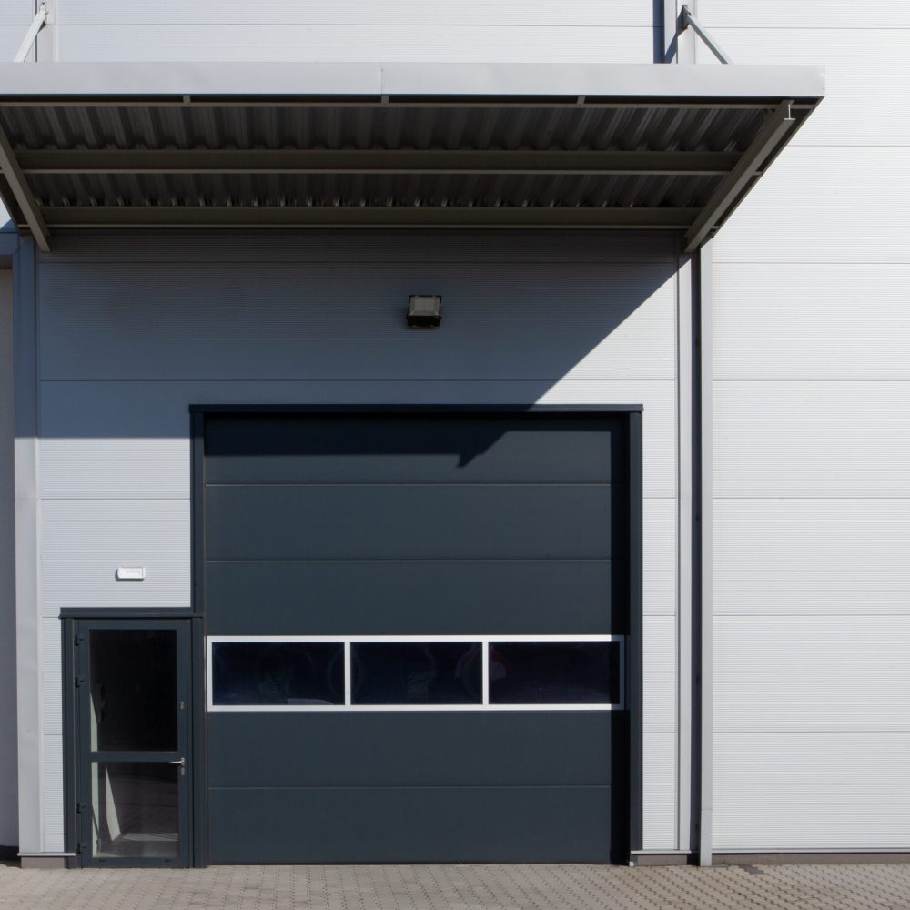 Detalj av verkstadshall i plåtfasad Detalj av verkstadshall med port, dörr och plåtfasad – exempel på modern industribyggnad.